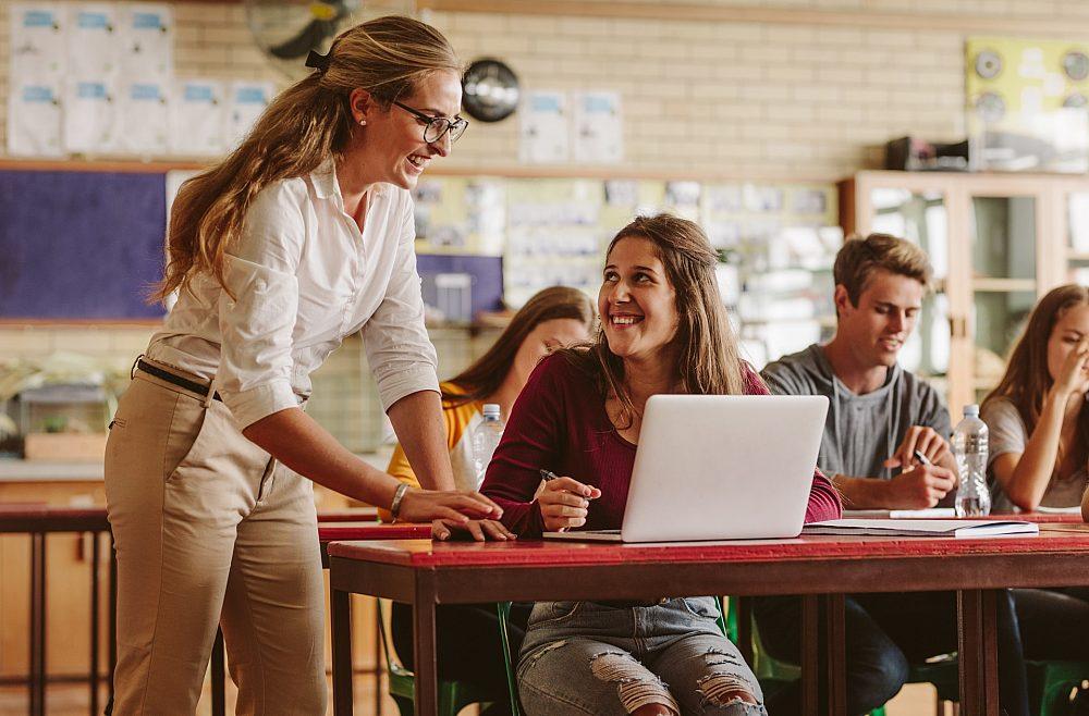 woman standing helping woman sitting work on her computer
