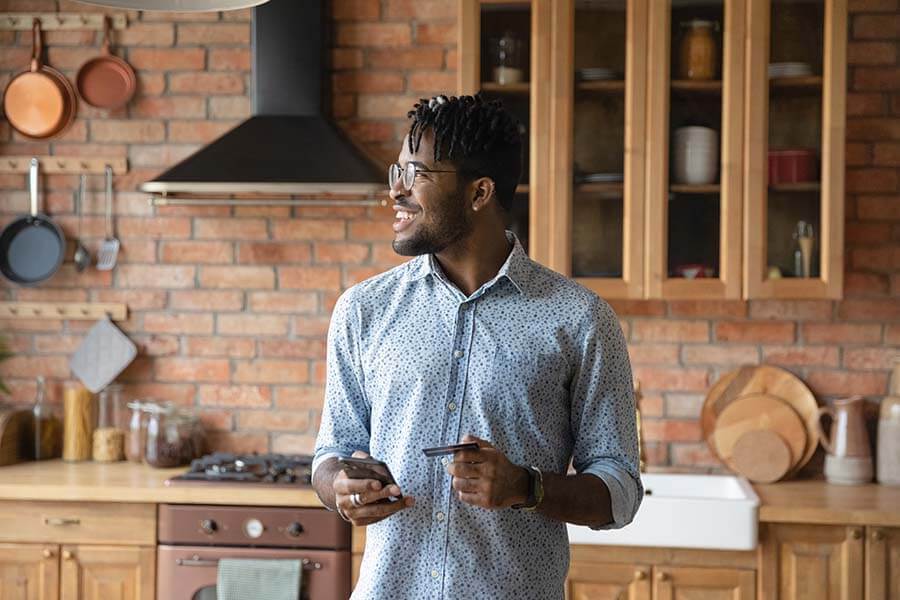 man smiling in a kitchen holding his card and a phone