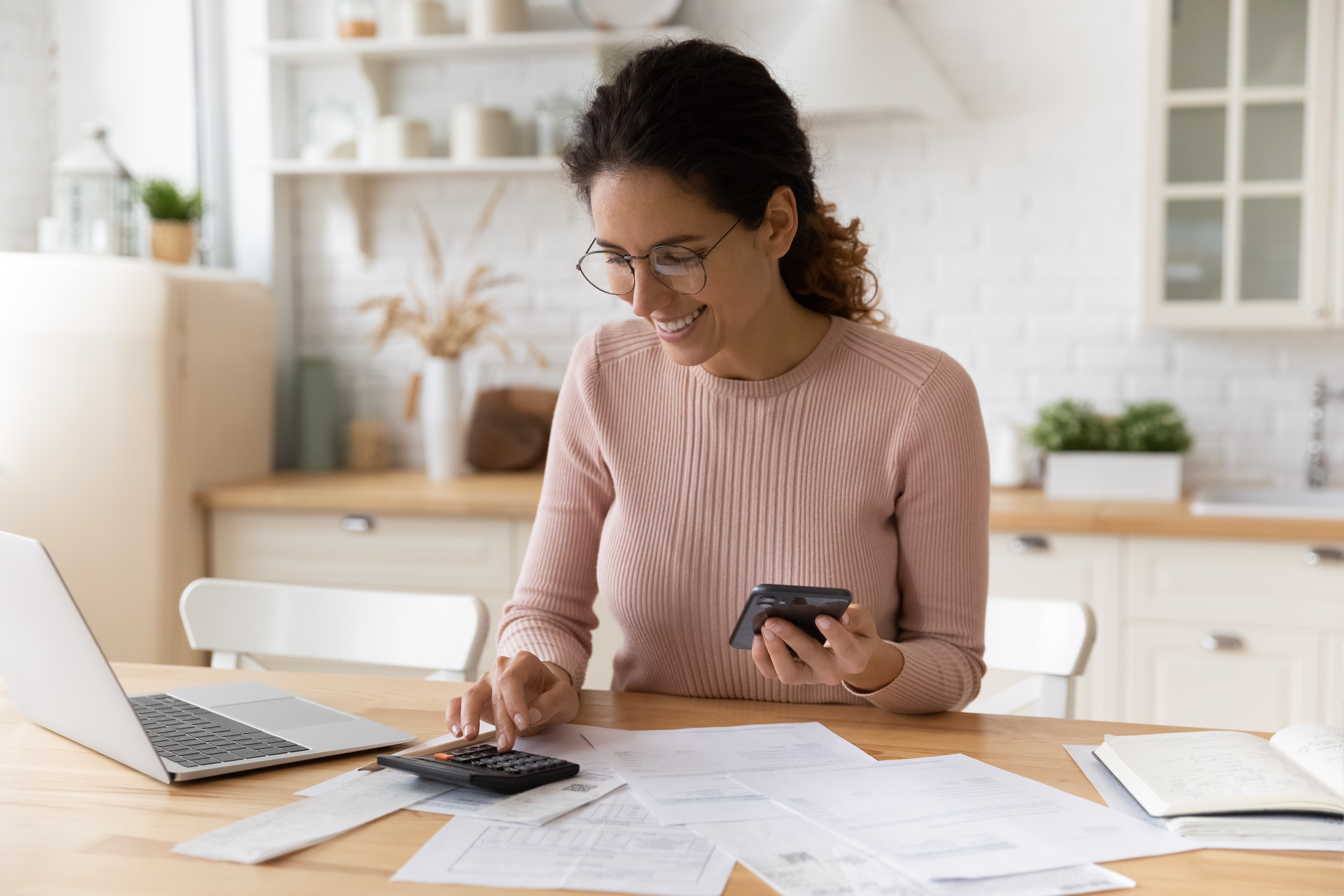 woman smiling at a desk typing on a calculator
