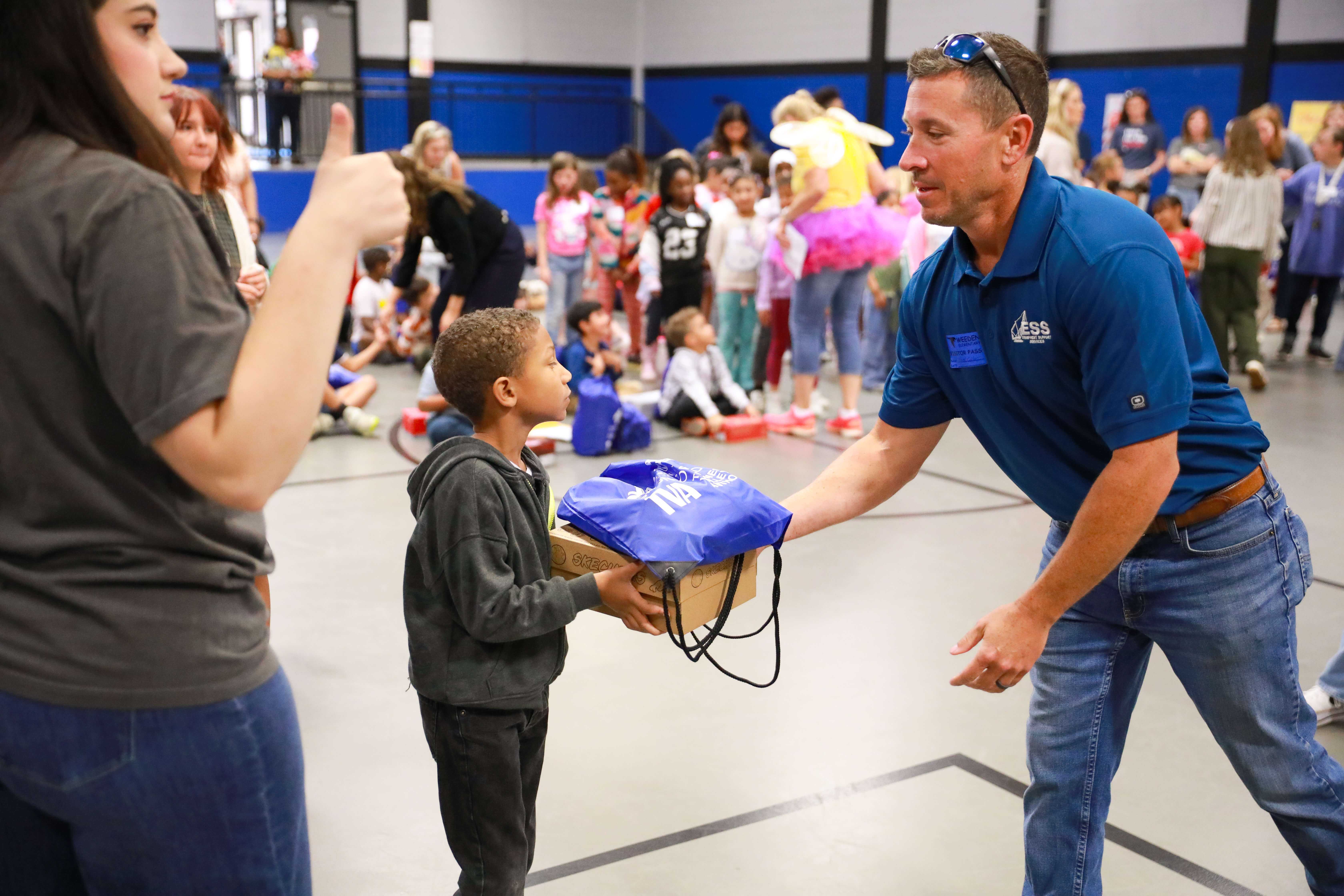 A Tennessee Valley Authority (TVA) employee hands brand new shoes and five pairs of Bombas socks to a Weeden Elementary student.